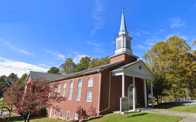 Red brick church with a white steeple and arched windows on a sunny autumn day.