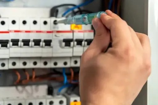 Electrician testing circuit breaker connections with a tester screwdriver inside an electrical panel.