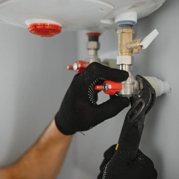 a professional technician wearing protective black grip gloves uses a specialized wrench to adjust a brass valve and pressure fittings during a comprehensive boiler repair in reston va.