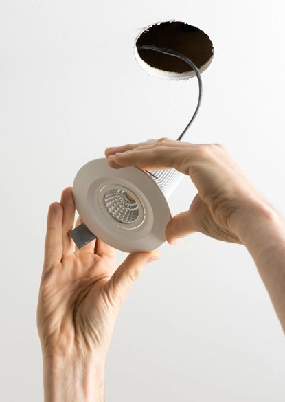 Technician aligning a new white LED recessed light into a ceiling opening as part of comprehensive LED lighting services in Springfield Virginia.
