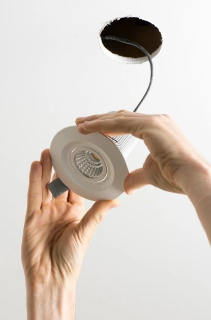 A technician's hands carefully aligning a white LED recessed light fixture into a ceiling opening during a professional recessed lighting installation in Reston VA.