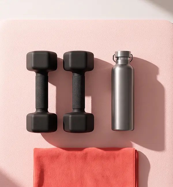 isão aérea de dois halteres pretos de musculação, uma garrafa térmica de metal prata e uma toalha coral dobrada sobre um colchonete de yoga rosa claro.