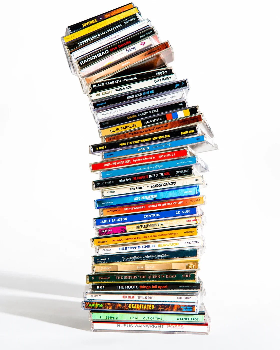 A tall, precarious stack of music CDs in their jewel cases stands upright against a white background. The stack leans slightly to the right, with the top CDs appearing to be on the verge of toppling over. The spines of the CDs are visible, displaying various album titles and artist names in different colors and fonts.