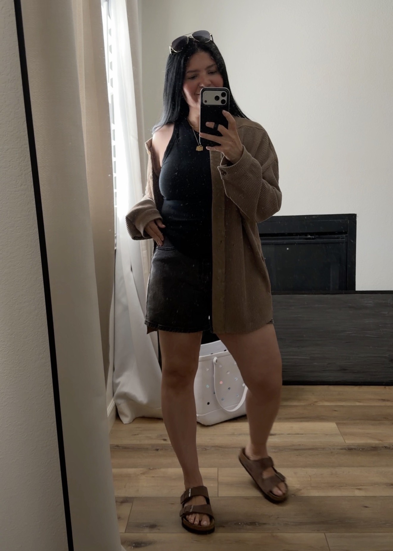 Mom in a neutral button, black tank, black shorts and Birkenstocks standing in front of the mirror