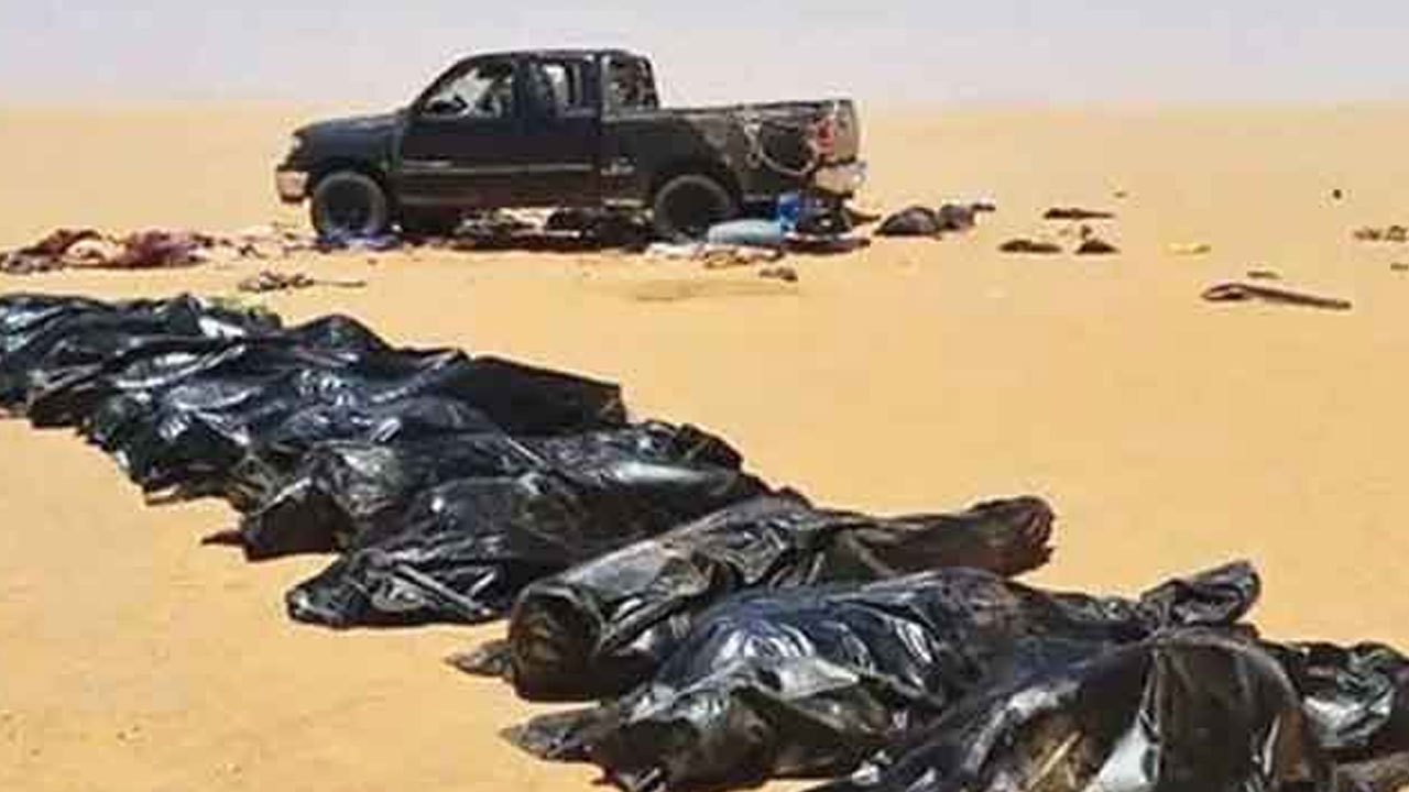 Desert scene with a black pickup truck in the distance and a row of black body bags laid out on the sand, suggesting a casualty site.