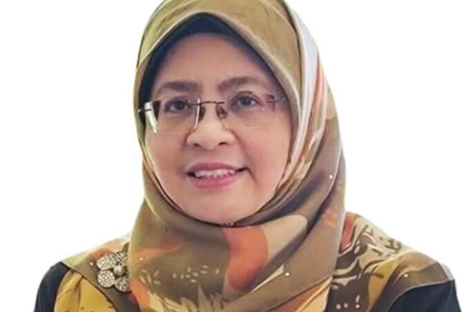 Portrait of a smiling woman wearing a brown and gold patterned hijab and glasses, facing the camera.
