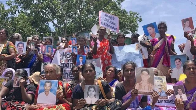Group of men and women at an outdoor protest, holding up portraits of missing loved ones amid banners and signs.