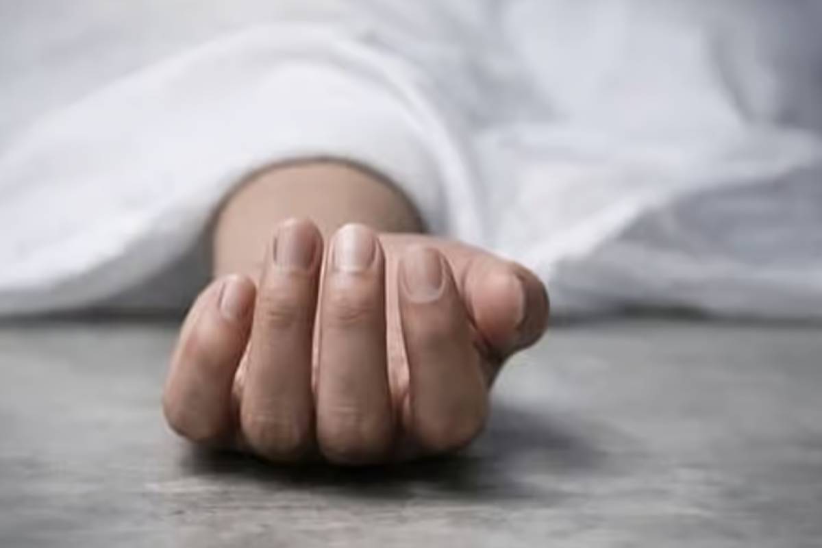 Close-up of a pale hand resting on a gray floor, with a white sheet in the background and fingers slightly curled.