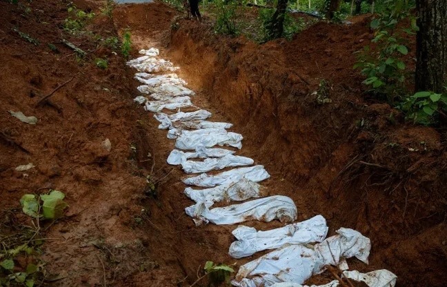 Line of white sandbags forming a narrow trench path through a muddy forest.