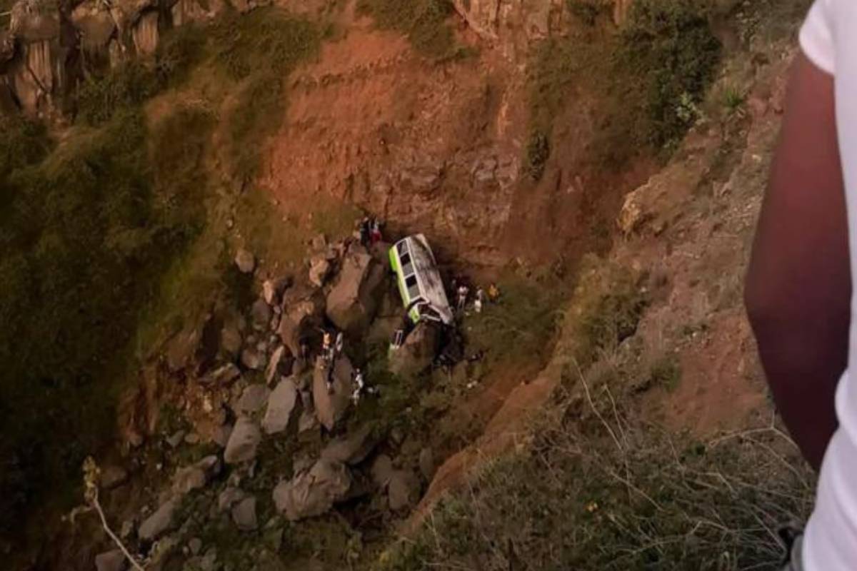 SUV or van crashed on a rocky hillside with people gathered around the wreckage.
