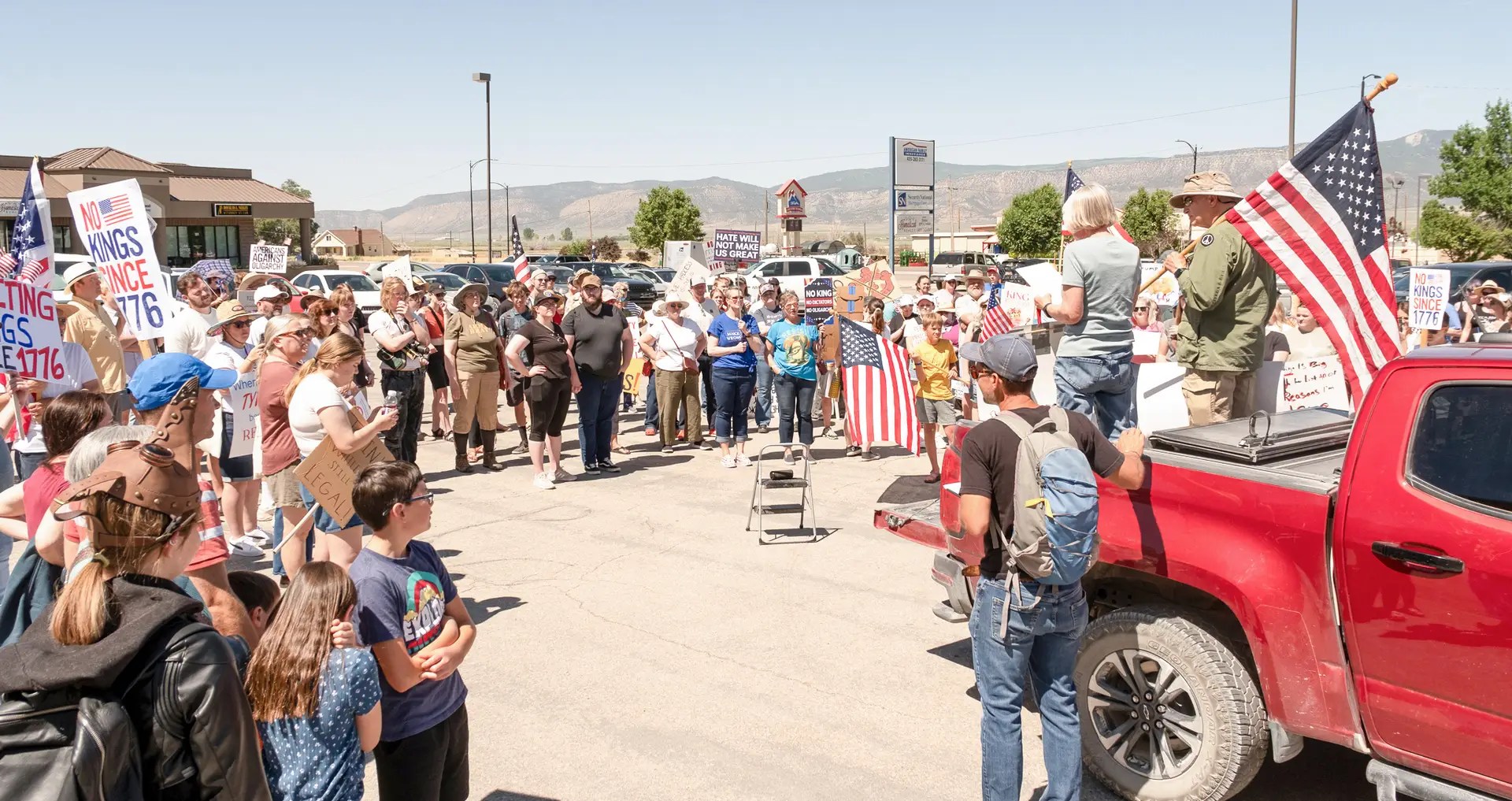 A group of people standing around a truck with a woman standing on the trunk. The people are holding protest signs.
