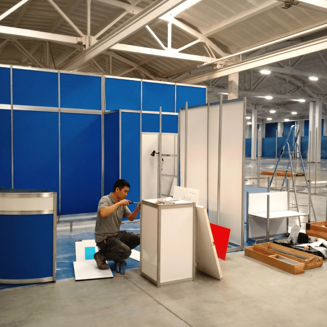 A man adjusts a display in a spacious room filled with various equipment and furniture.