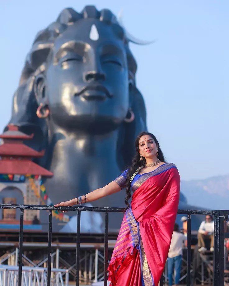 Rithu Manthra in a pink and red silk saree near the Adiyogi statue.