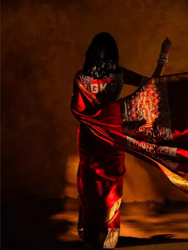 Silhouette shot of Aishwarya Lekshmi in a custom red silk saree, holding the pallu dramatically under warm golden light.