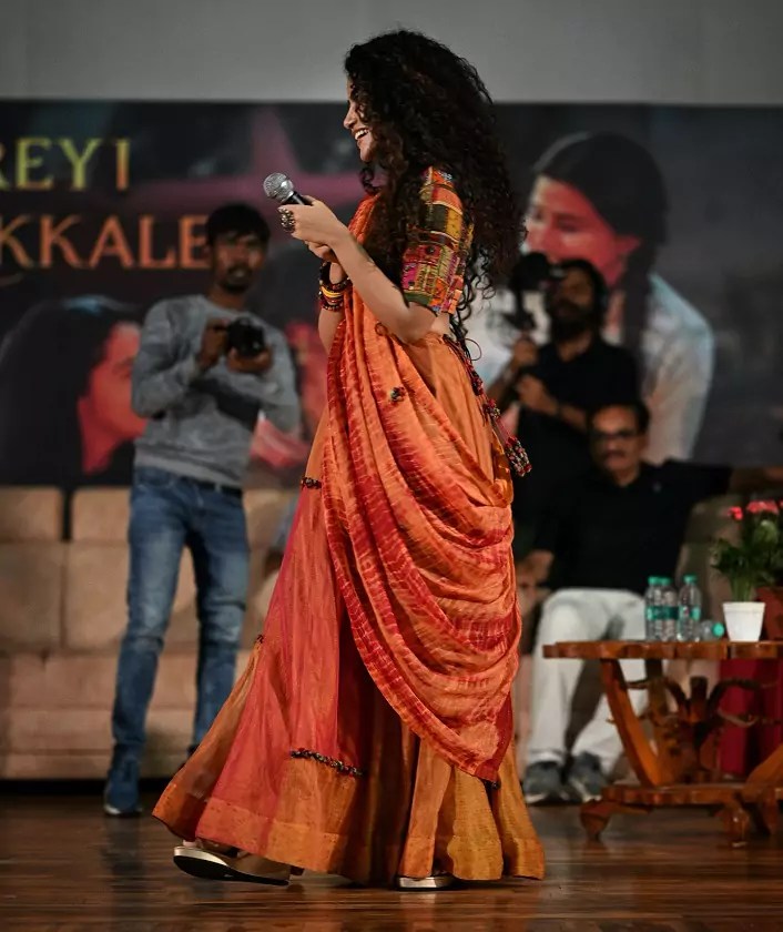 Anupama Parameswaran’s side view in orange saree at an event.