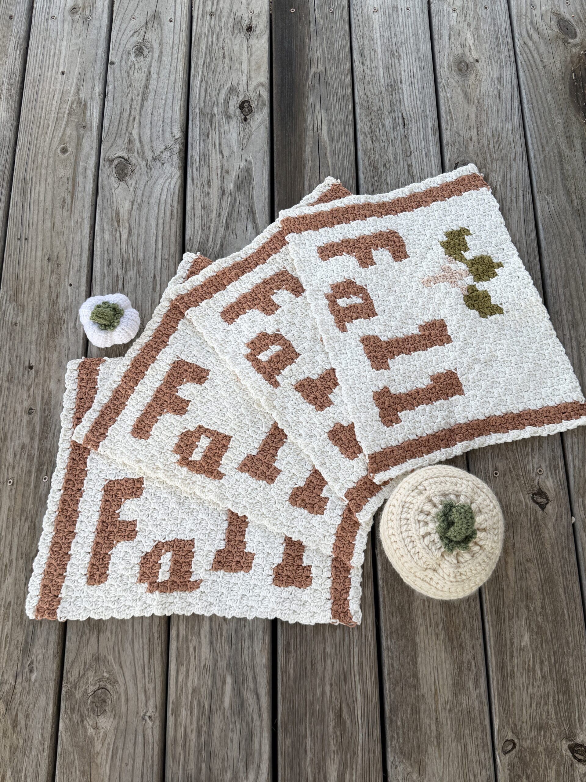 Three FALL Farmhouse crochet placemats arranged on a wooden table with small crocheted pumpkins.