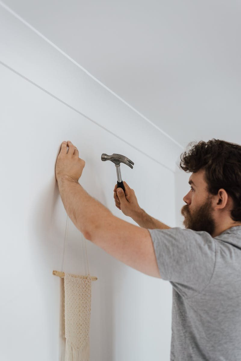 Side view of bearded craftsman with hammer putting decoration on wall during renovation works
