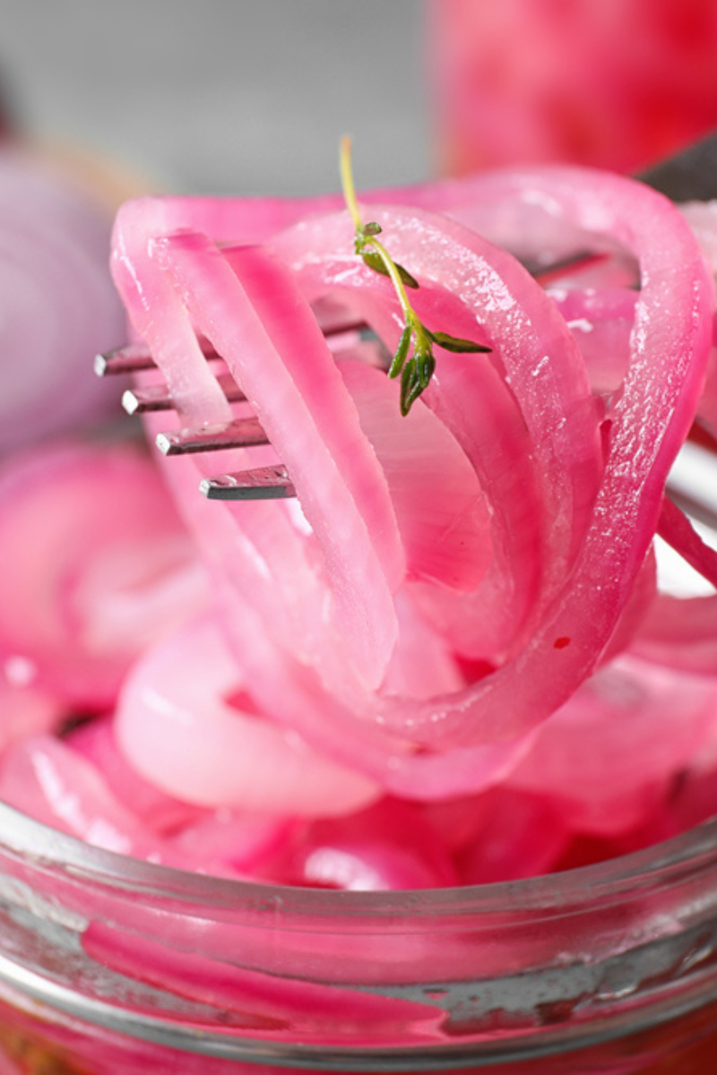 pickled red onion in mason jar. Fork with onion and sprig of thyme hovering over it