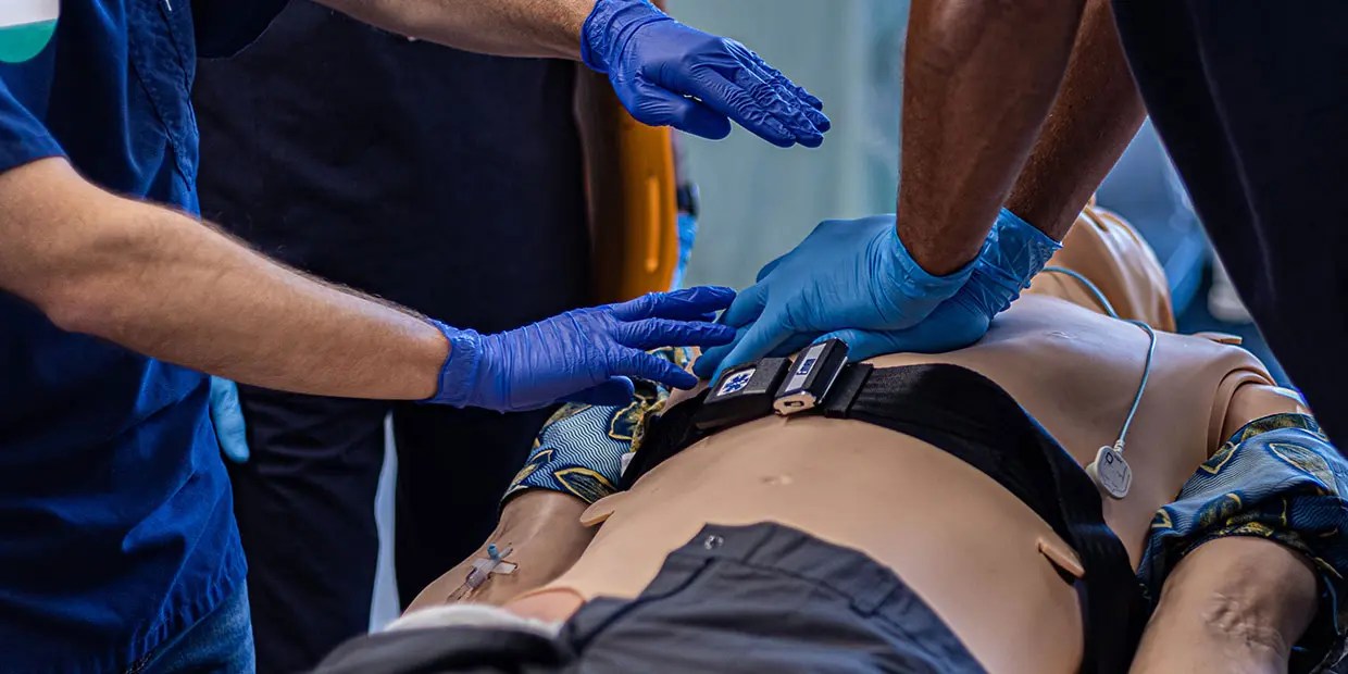 Students practicing emergency medical procedures on a training mannequin during a BPPE-approved EMT program.