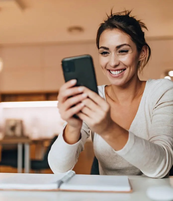 A school owner smiling while checking her BPPE application approval status on a smartphone.