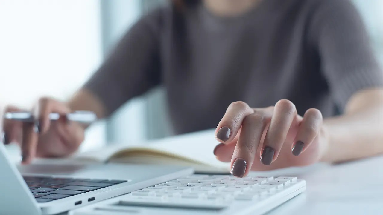 Hands using a calculator and laptop to review school costs.