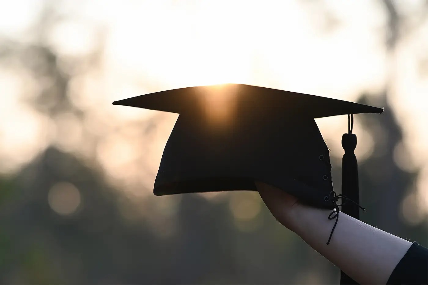 Graduation cap held up against a sunset sky.