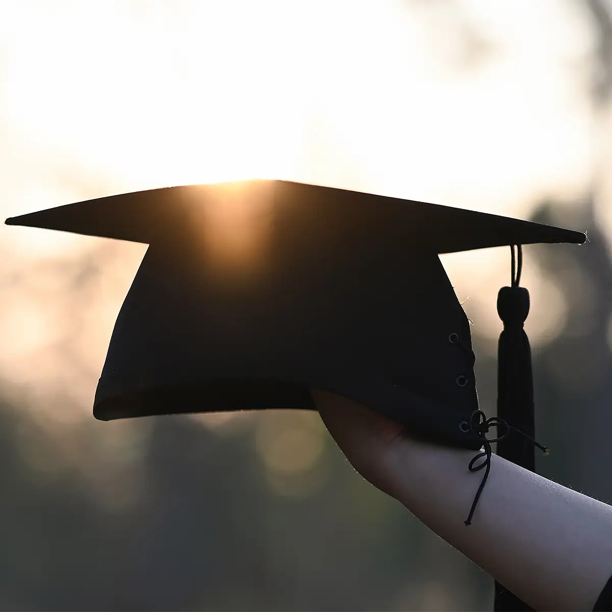 Graduation cap held up against a sunset sky.