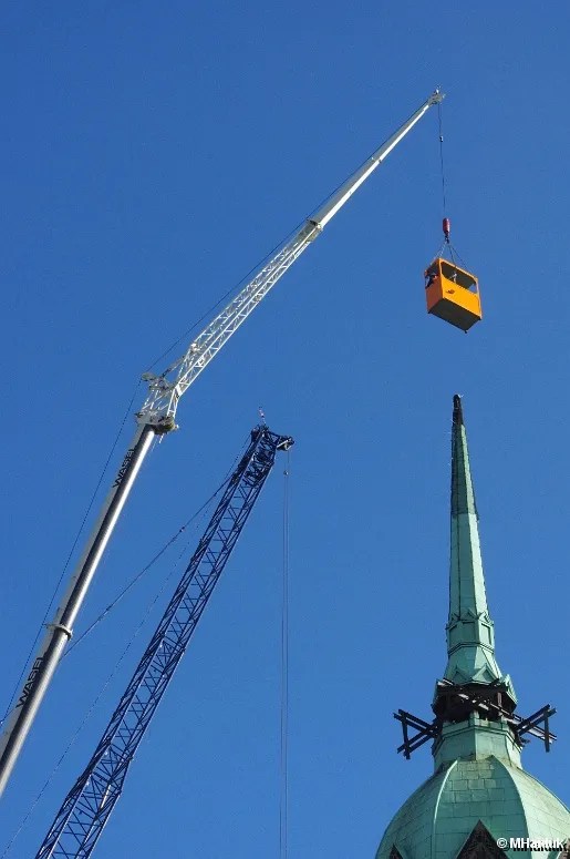 eleskopkran mit Wippspitze hebt eine Arbeitsplattform neben einen Kirchturm.