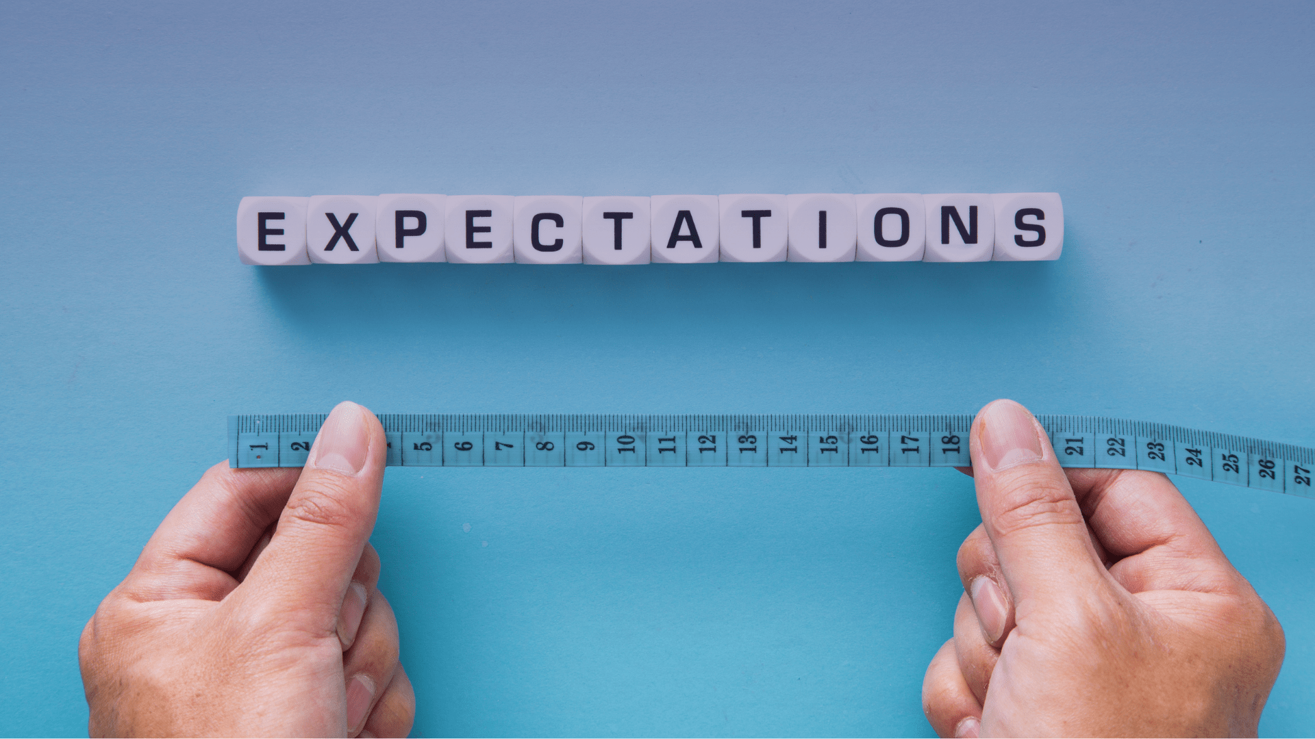 The word 'expectations' is spelled out in blocks and a person holds a tape measure.
