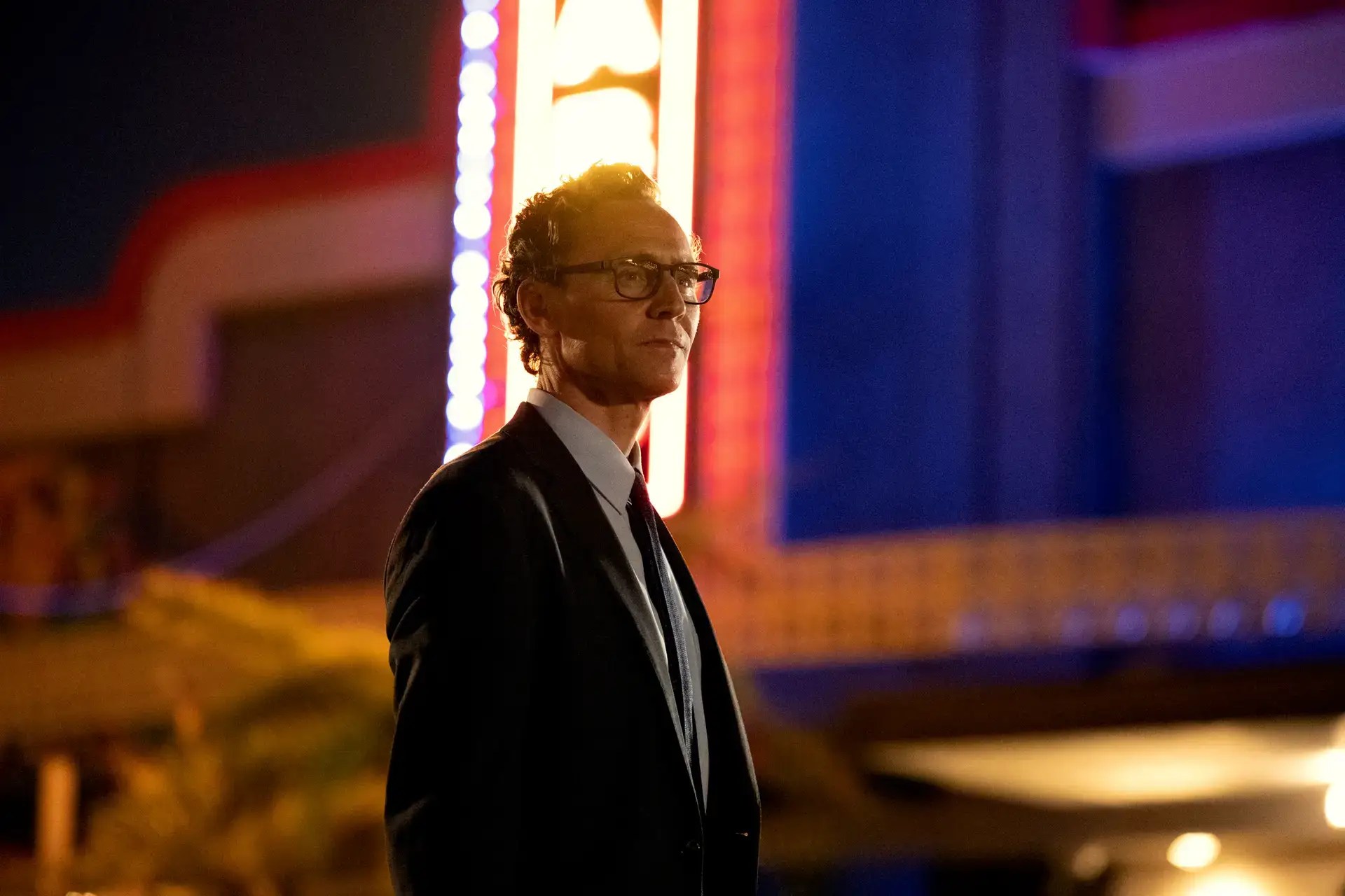 Actor Tom Hiddleston in The Life of Chuck film standing in front of a theater marquee at night