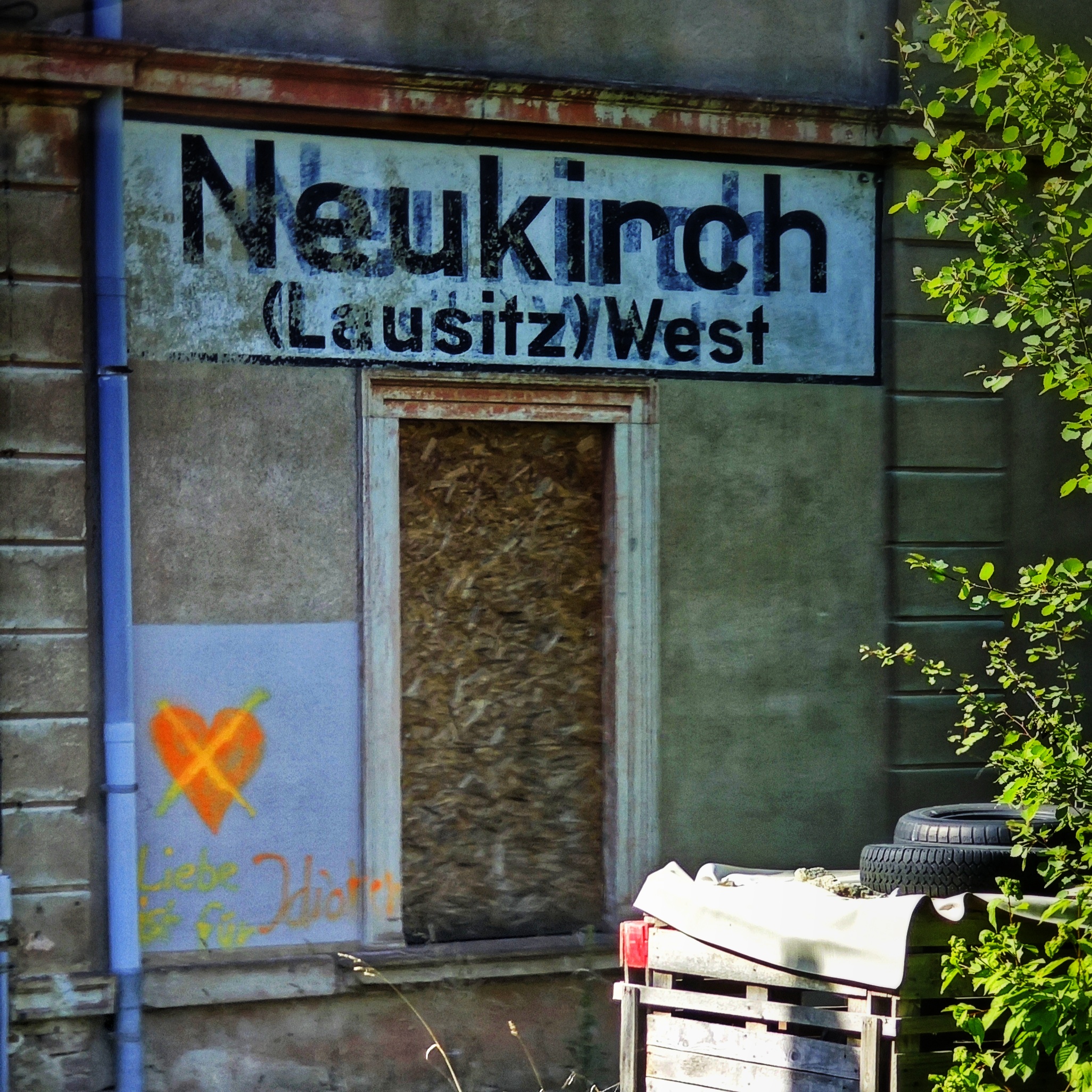 Auf einer Seite des Bahnhofsgebäudes von Neukirch (Lausitz) West ist ein Herz in Neonorange gemalt. Es ist mit einem neongelben X durchgestrichen. Darunter steht: "Liebe ist für Idioten".