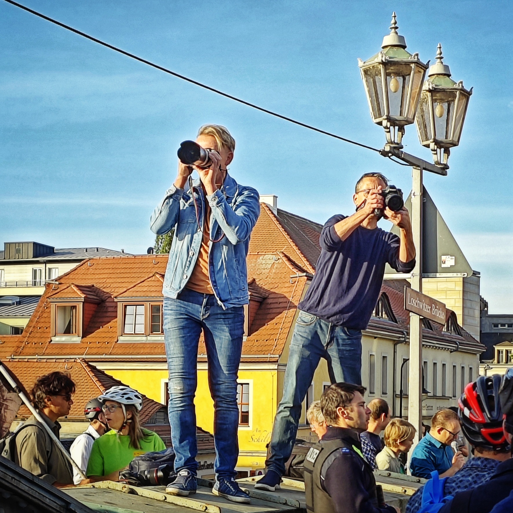Zwei Fotografen stehen etwas erhöht über Menschen und fotografieren in die Menge hinein.