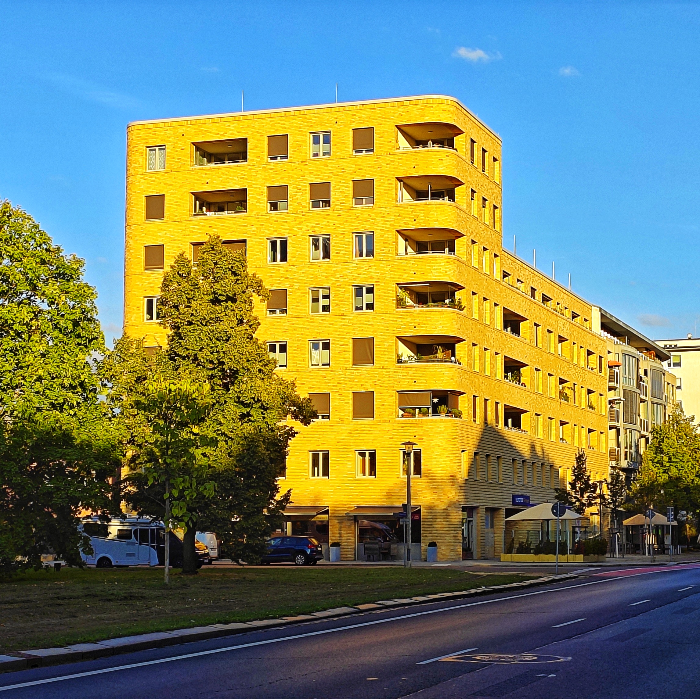 Moderner Wohnkomplex nach Stil des Bauhauses mit abgerundeten Balkonen, der im Abendlicht gelb leuchtet.