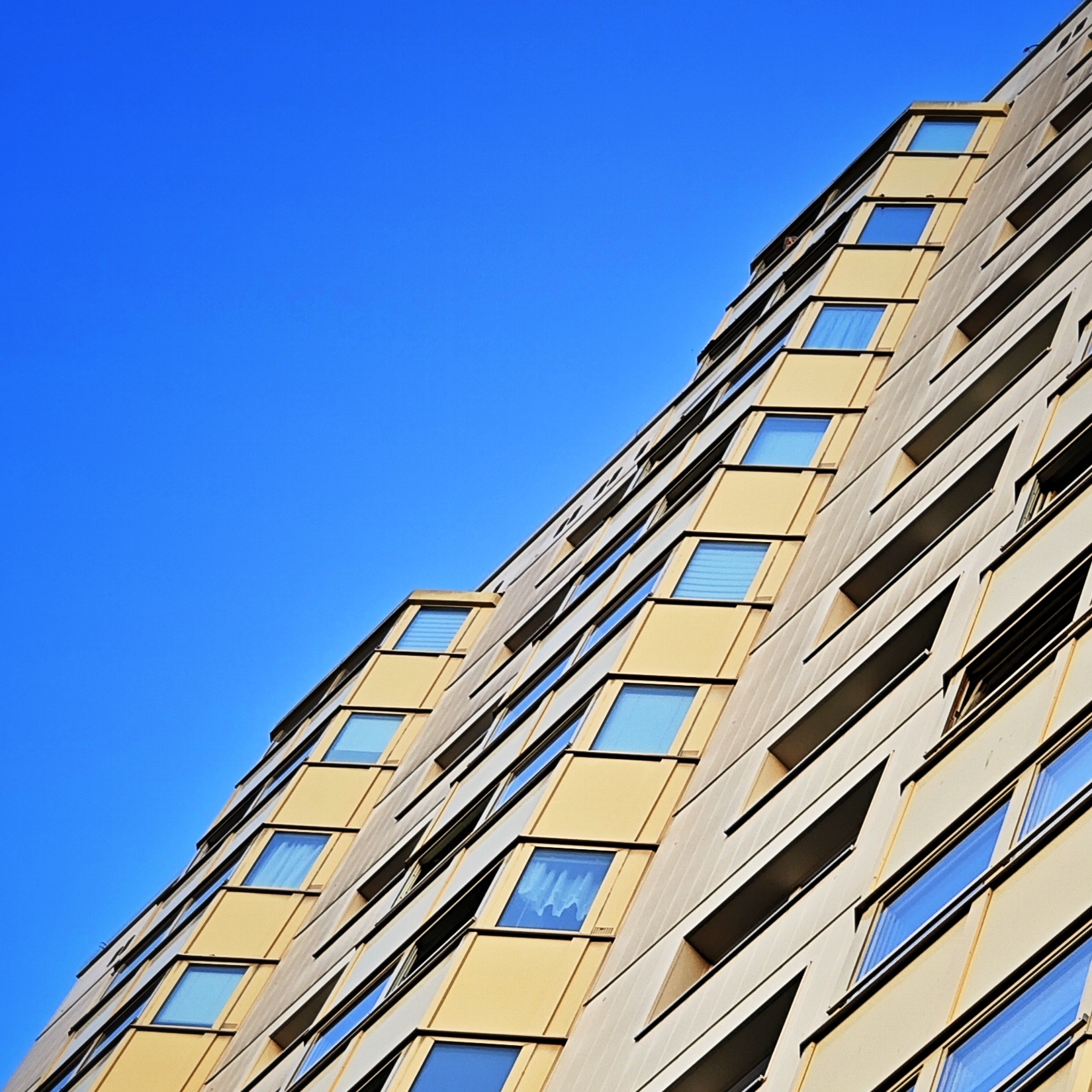 Hochhausfassade im schrägen Profil, von unten nach oben fotografiert. Der blaue Himmel bildet die andere diagonale Hälfte des Bildes.