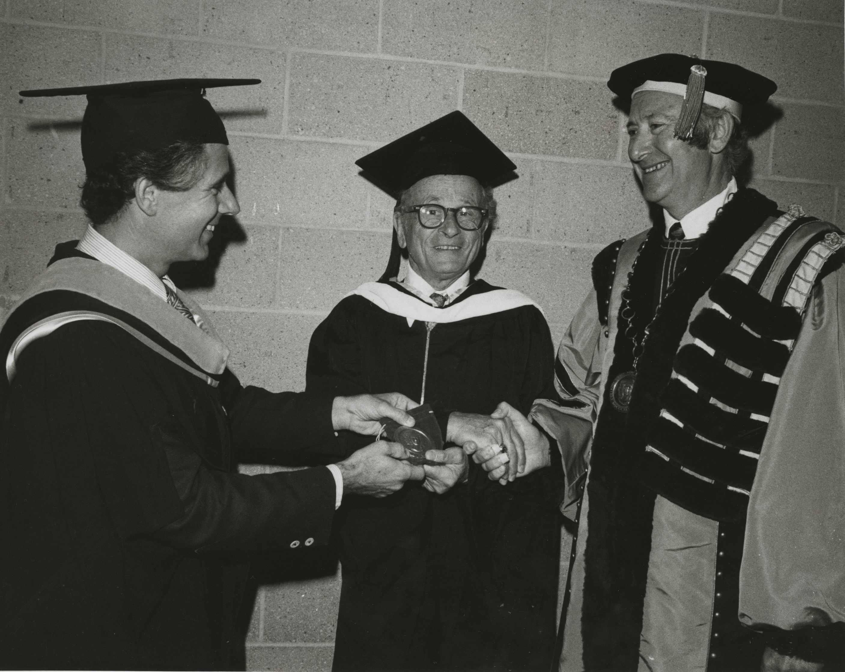 Marshak, dressed in regalia, shakes hands with two other men, also in regalia, as he receives an award.