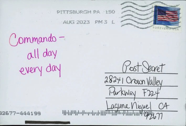 A postcard with handwritten text in pink ink, featuring an American flag stamp.
