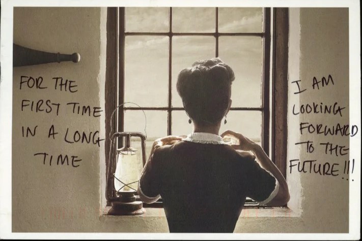 A person in a vintage dress looks out a window, with a lantern beside them.
