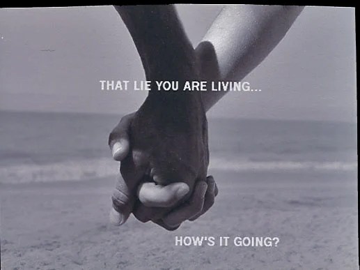 A monochrome photograph of two hands clasped together against a beach backdrop.