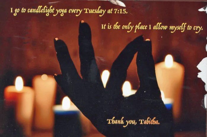 A silhouette of a hand in a yoga gesture against a backdrop of candles, creating a serene atmosphere.
