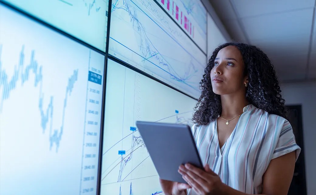 Businesswoman holding a tablet and analyzing charts on interactive digital screens, representing centralized security data and streamlined audit preparation.