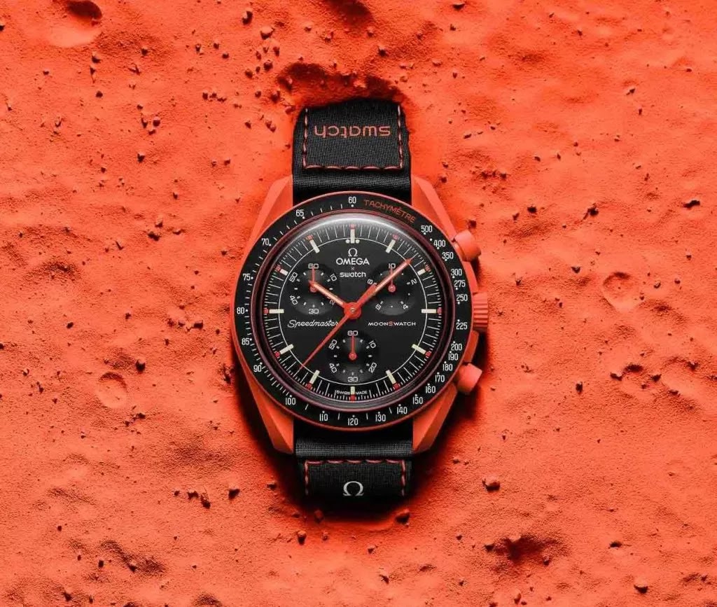 An Omega x Swatch Speedmaster watch placed on a textured orange surface resembling the moon's surface.