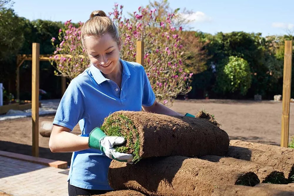 A young woman wears glove while lifting a roll of grass