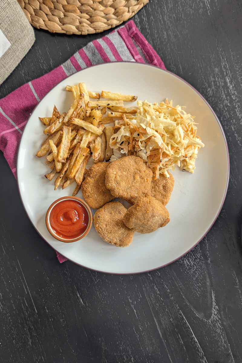 chicken nugget disajikan diatas piring dengan kentang goreng dan coleslaw