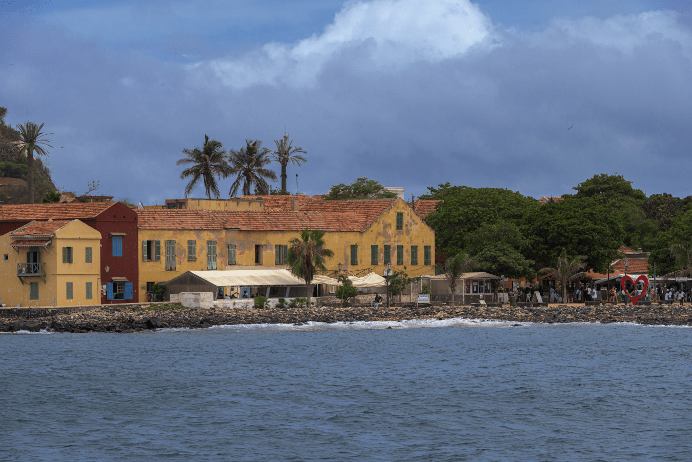 Vista de la isla Gorée desde el barco, al fondo sus casas de colores , palmeras y el monumento al Amor, el corazón
