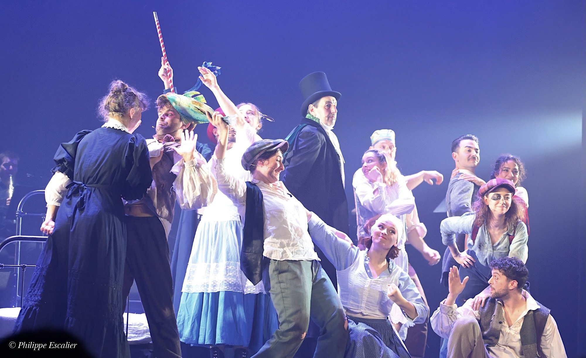 Groupe d'acteurs en costume sur scène, exprimant des émotions variées dans une performance théâtrale.