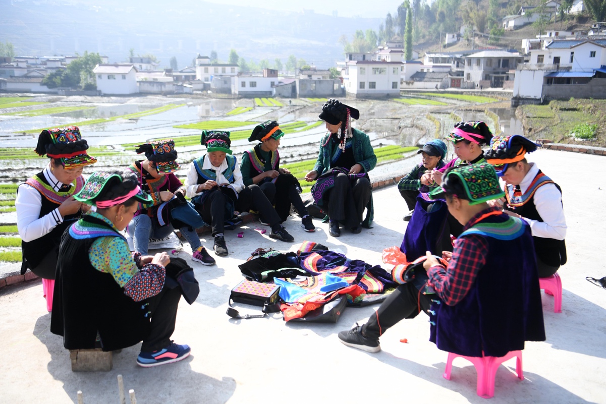 （2）4月15日，四川甘洛县普昌镇哈木觉村，省级非遗项目彝族传统刺绣技艺传承人阿西巫之莫（右五）指导彝族绣娘。刘忠俊 摄