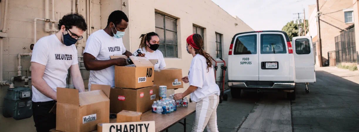 Volunteers in masks packing charity donation boxes beside a van