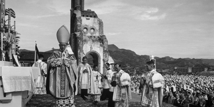 Cerimônia religiosa com bispos e sacerdotes diante das ruínas da cidade de Hiroshima, com grande parte da população reunida para um evento solene.