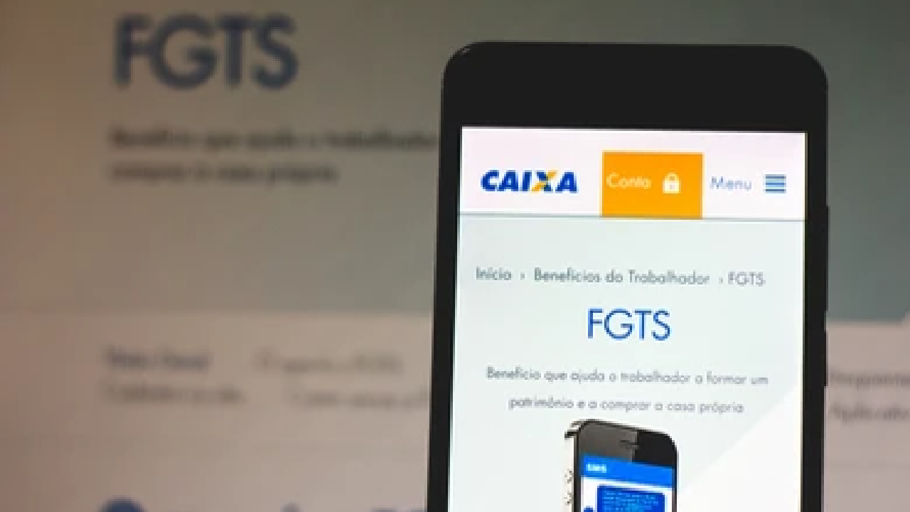 Celular mostrando na tela a página do FGTS no site da Caixa. Ao fundo, uma tela maior mostra a mesma página.