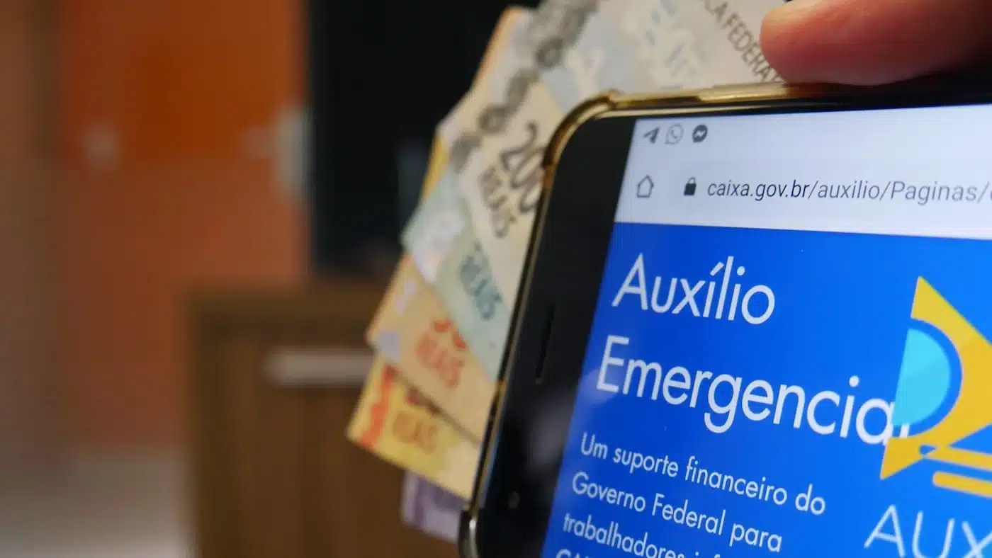 novo auxílio emergencial indicado por notas de dinheiro e o app da Caixa aberto